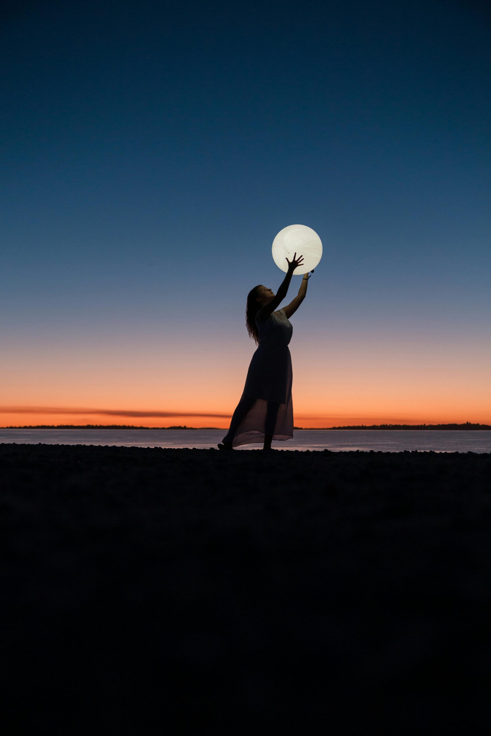 A serene scene of a woman silhouetted against a sunset sky, reaching towards the full moon.